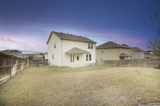 back house at dusk with a patio and a lawn