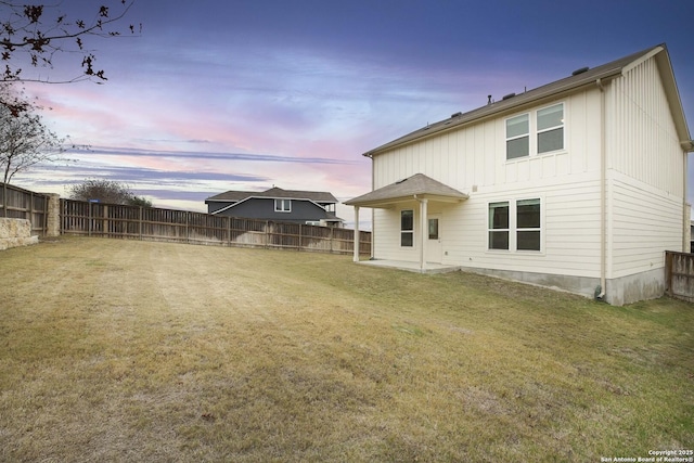 back house at dusk featuring a yard and a patio area