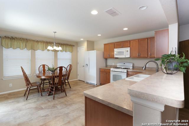 kitchen featuring sink, white appliances, a notable chandelier, decorative light fixtures, and kitchen peninsula