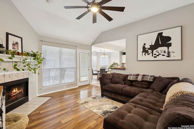 living room featuring ceiling fan with notable chandelier, light hardwood / wood-style flooring, a tile fireplace, and vaulted ceiling