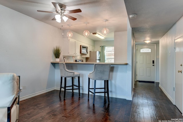 kitchen featuring a breakfast bar, decorative light fixtures, appliances with stainless steel finishes, kitchen peninsula, and white cabinets