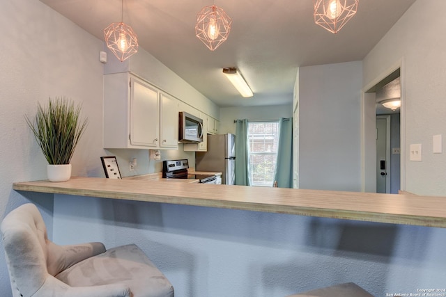 kitchen with appliances with stainless steel finishes, hanging light fixtures, and white cabinets