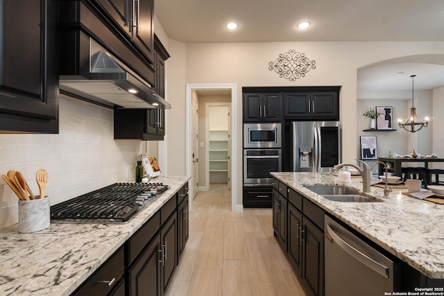 kitchen with appliances with stainless steel finishes, pendant lighting, sink, backsplash, and exhaust hood