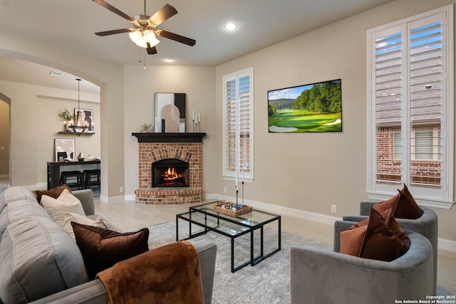 living room with a brick fireplace, ceiling fan with notable chandelier, and light hardwood / wood-style floors