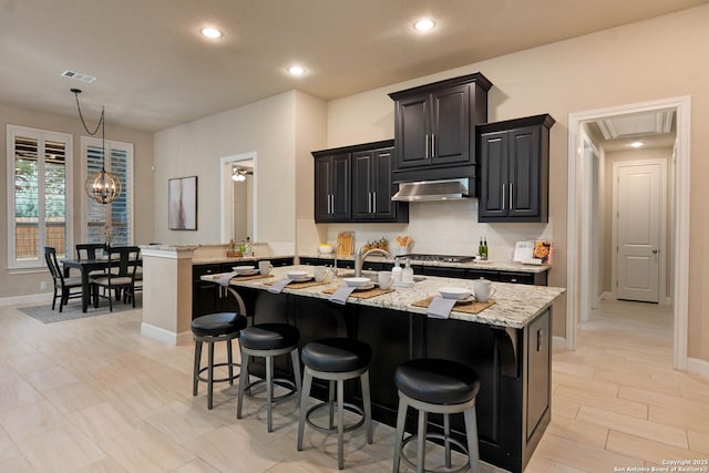 kitchen with light stone countertops, a breakfast bar area, and a center island with sink