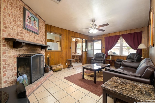 living room featuring ceiling fan, wood walls, a brick fireplace, and light tile patterned floors