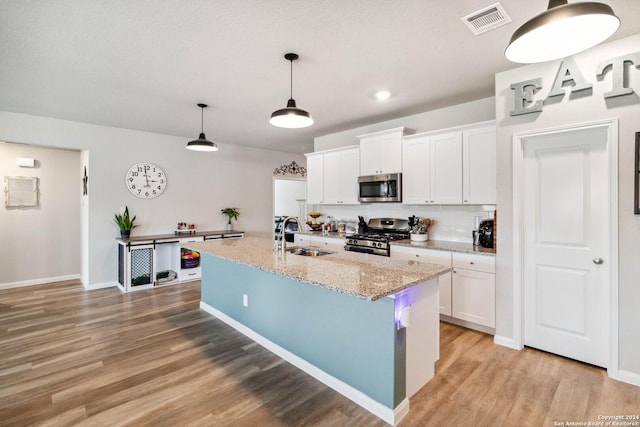 kitchen featuring pendant lighting, an island with sink, white cabinets, light stone counters, and stainless steel appliances