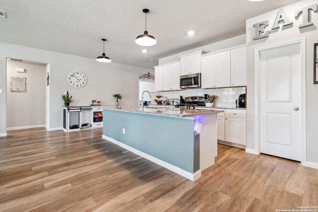 kitchen featuring white cabinetry, an island with sink, hanging light fixtures, stainless steel appliances, and light stone countertops