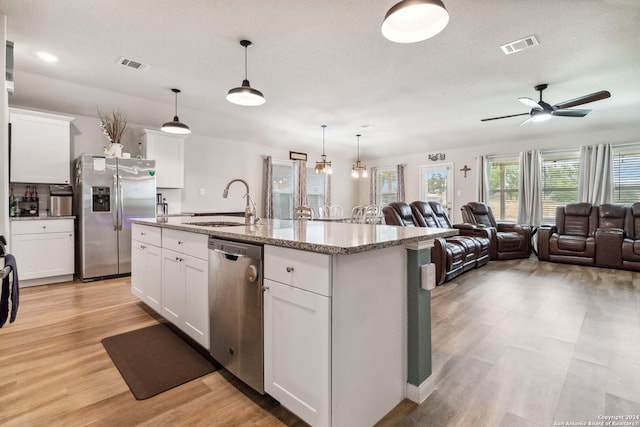 kitchen with stainless steel appliances, white cabinetry, a center island with sink, and decorative light fixtures