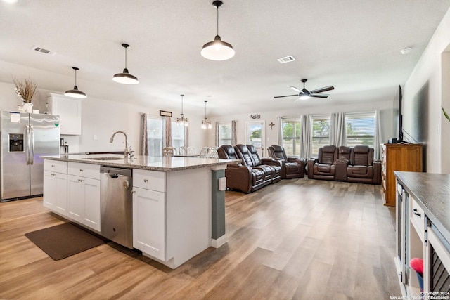 kitchen featuring sink, appliances with stainless steel finishes, hanging light fixtures, an island with sink, and white cabinets