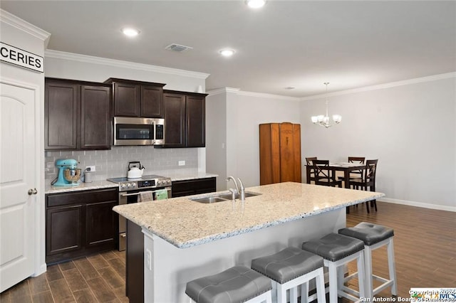 kitchen with appliances with stainless steel finishes, decorative light fixtures, an island with sink, sink, and dark hardwood / wood-style flooring