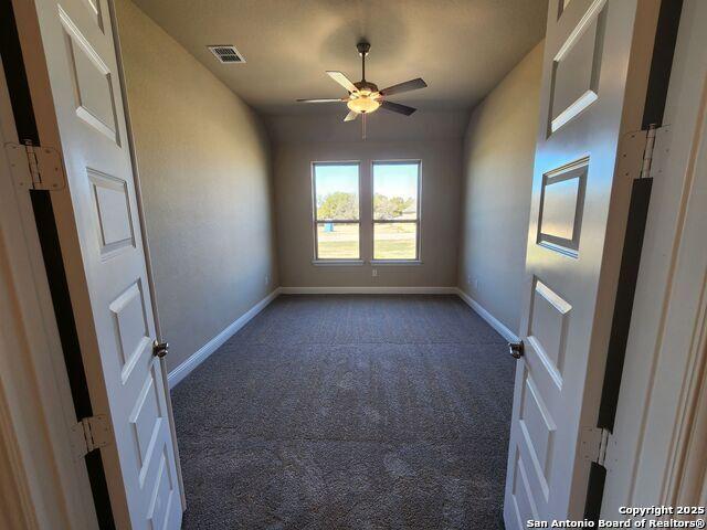 unfurnished room with dark carpet and ceiling fan