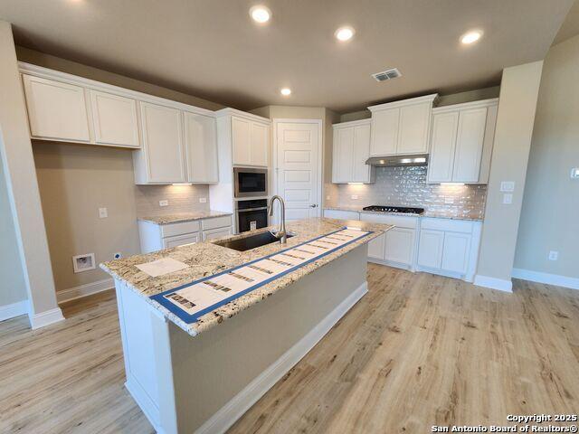 kitchen with sink, light hardwood / wood-style floors, an island with sink, white cabinets, and built in microwave