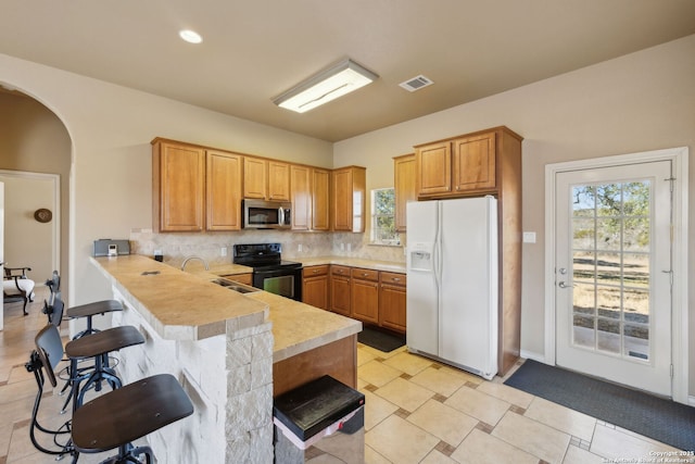 kitchen with tasteful backsplash, a kitchen bar, white refrigerator with ice dispenser, kitchen peninsula, and black / electric stove