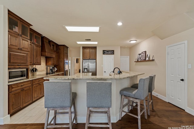 kitchen with a kitchen bar, custom exhaust hood, light hardwood / wood-style floors, stainless steel appliances, and a spacious island