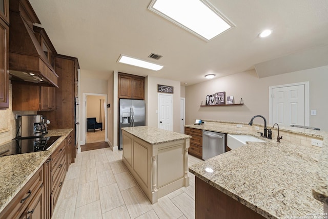 kitchen with a spacious island, sink, light stone counters, custom range hood, and stainless steel appliances