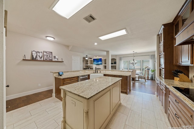 kitchen featuring pendant lighting, sink, dishwasher, light stone countertops, and a kitchen island