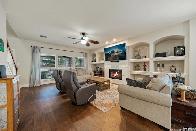 living room with built in shelves, dark wood-type flooring, and ceiling fan