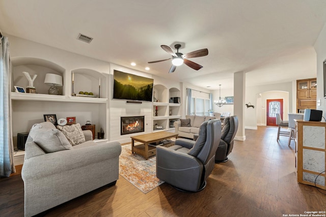 living room featuring built in shelves, ceiling fan with notable chandelier, and hardwood / wood-style flooring