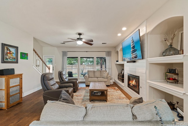 living room with dark wood-type flooring, a large fireplace, and ceiling fan