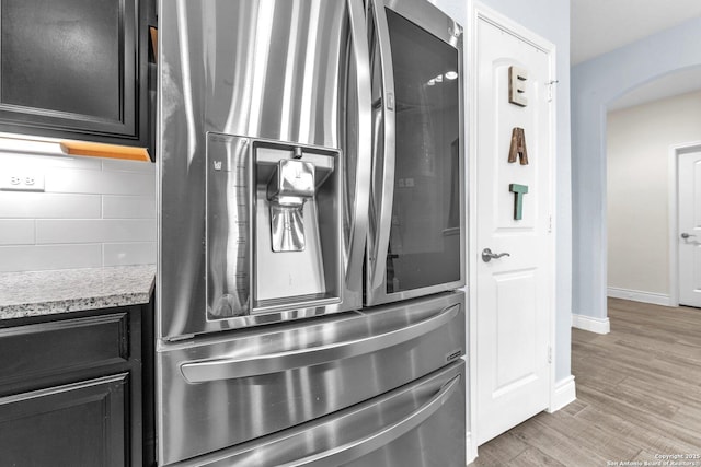 details featuring tasteful backsplash, light stone counters, light wood-type flooring, and stainless steel refrigerator with ice dispenser