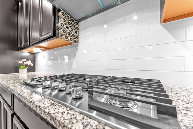 room details featuring dark brown cabinets, stainless steel gas cooktop, backsplash, and dark stone counters