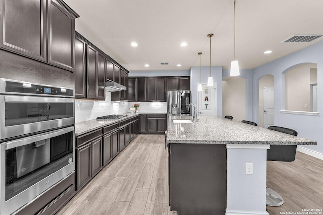 kitchen with a spacious island, a kitchen bar, decorative light fixtures, stainless steel appliances, and backsplash