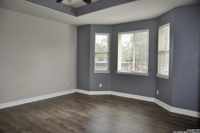 empty room featuring ceiling fan, a tray ceiling, and dark hardwood / wood-style floors