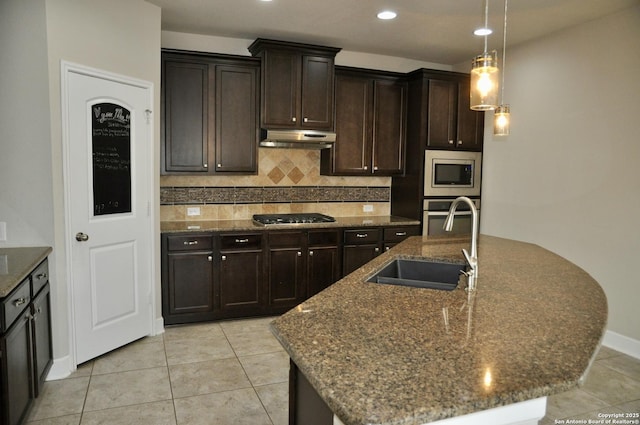 kitchen featuring sink, a kitchen island with sink, stainless steel appliances, tasteful backsplash, and dark brown cabinetry