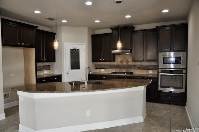 kitchen with sink, tasteful backsplash, hanging light fixtures, appliances with stainless steel finishes, and a kitchen island with sink