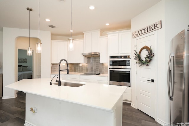 kitchen featuring appliances with stainless steel finishes, decorative light fixtures, white cabinetry, sink, and a center island with sink