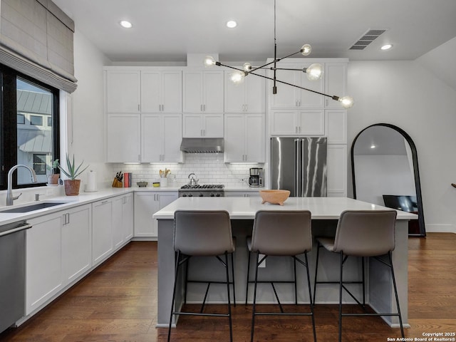 kitchen featuring pendant lighting, sink, white cabinetry, stainless steel appliances, and a center island