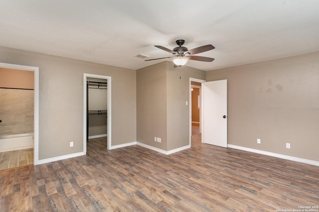 unfurnished bedroom with connected bathroom, hardwood / wood-style flooring, a walk in closet, ceiling fan, and a closet