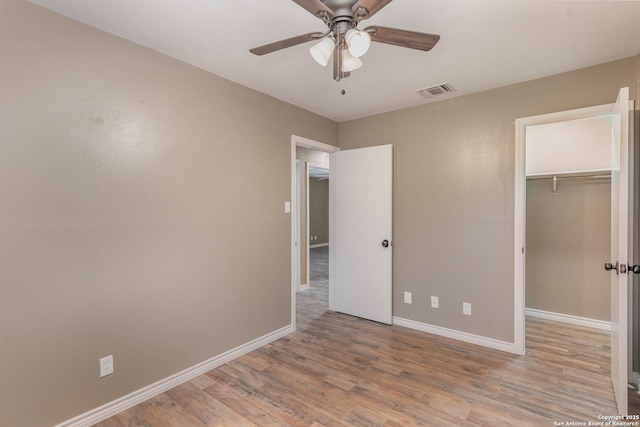 unfurnished bedroom with ceiling fan, a spacious closet, light hardwood / wood-style floors, and a closet