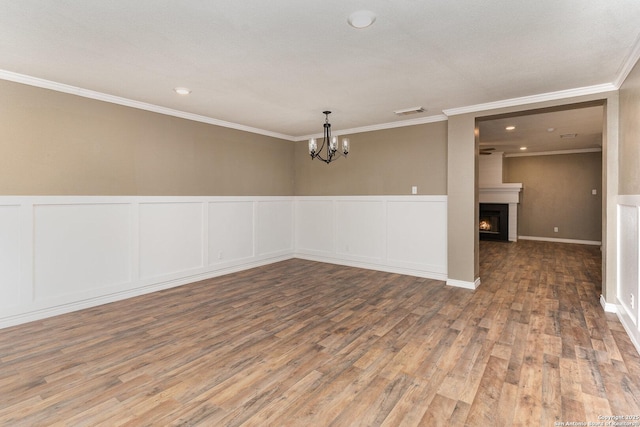 spare room with a notable chandelier, hardwood / wood-style flooring, a fireplace, and ornamental molding