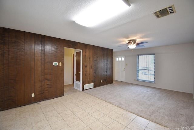 carpeted empty room featuring ceiling fan, wooden walls, and a textured ceiling