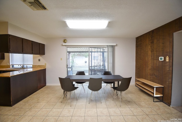 tiled dining room with sink, a textured ceiling, and wood walls