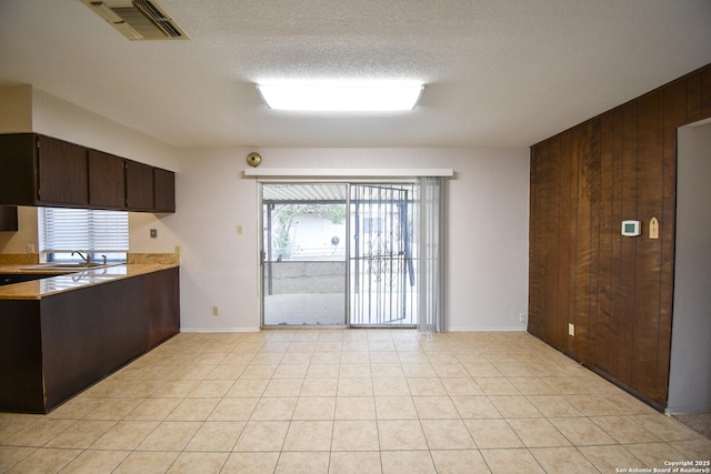 kitchen featuring light tile patterned flooring, wooden walls, sink, dark brown cabinetry, and a textured ceiling