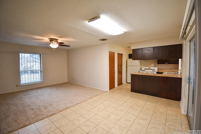 kitchen featuring dark brown cabinets, light carpet, kitchen peninsula, white fridge, and stove