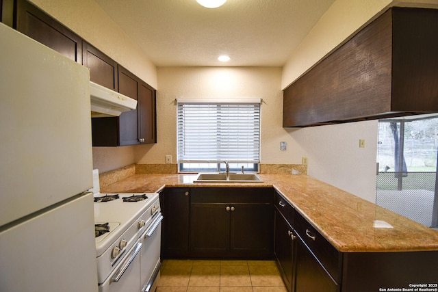 kitchen featuring sink, light tile patterned floors, dark brown cabinetry, kitchen peninsula, and white appliances