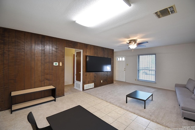 living room with light carpet, a textured ceiling, ceiling fan, and wood walls