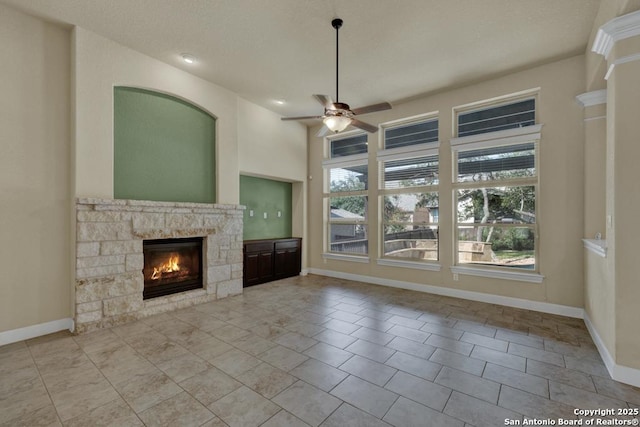 unfurnished living room featuring a stone fireplace and ceiling fan