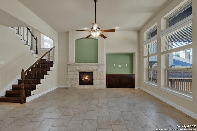 unfurnished living room with ceiling fan, plenty of natural light, a towering ceiling, and a fireplace