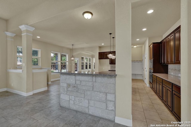 kitchen featuring pendant lighting, light stone counters, tasteful backsplash, and dark brown cabinets