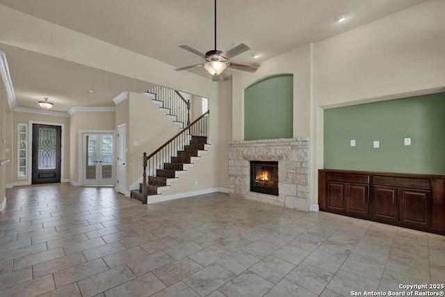 unfurnished living room featuring a towering ceiling, a fireplace, ceiling fan, crown molding, and french doors