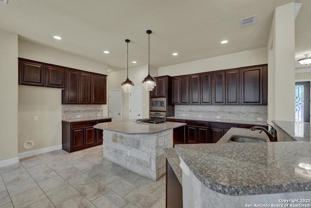 kitchen featuring dark brown cabinetry, sink, stainless steel microwave, a kitchen island, and pendant lighting