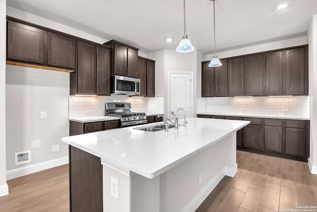 kitchen featuring sink, a kitchen island with sink, hanging light fixtures, stainless steel appliances, and dark brown cabinetry