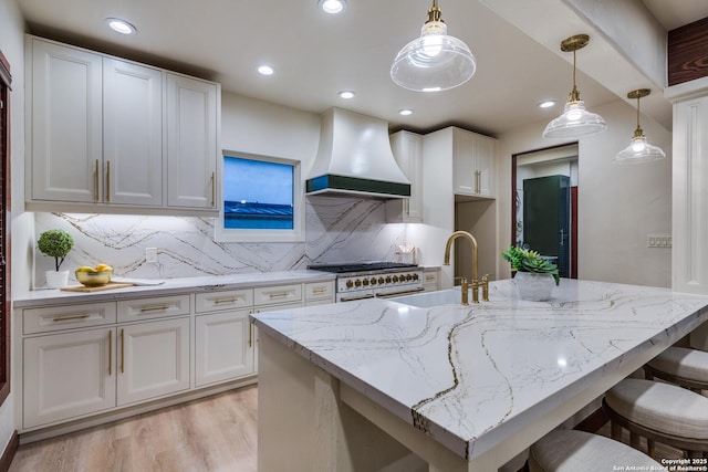 kitchen featuring white cabinets, custom exhaust hood, double oven range, hanging light fixtures, and light stone counters