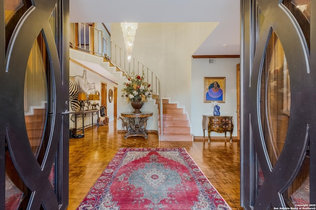 foyer entrance with crown molding, parquet flooring, and a notable chandelier