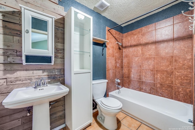 bathroom with tile patterned flooring, wooden walls, a textured ceiling, toilet, and tiled shower / bath